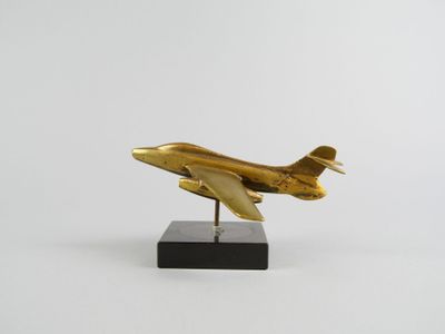 un avion doré posé sur un socle noir, sur fond blanc