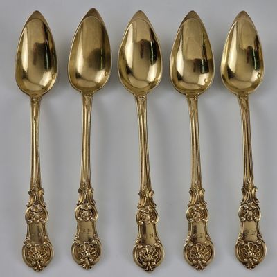 cinq cuillères en or aux motifs ouvragés sont alignées sur une surface blanche