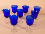 six verres à pied bleus sont alignés sur une surface blanche