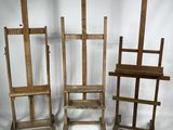 Trois chevalets en bois et une chaise sont disposés devant un fond blanc.