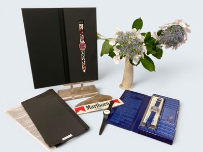 a vase with flowers and a watch on it next to a book and pen