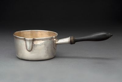 une saucière en argent avec une poignée noire sur un fond gris