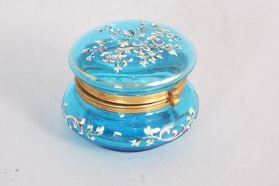 une boîte en verre bleue avec un couvercle doré, posée sur une surface blanche