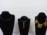 three black mannequins with gold and green jewelry on them