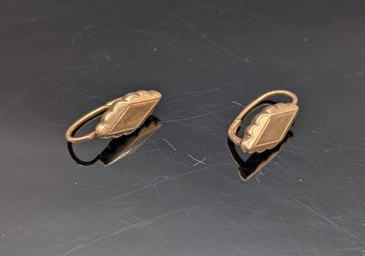 une paire de boucles d'oreilles dorées posées sur un fond noir
