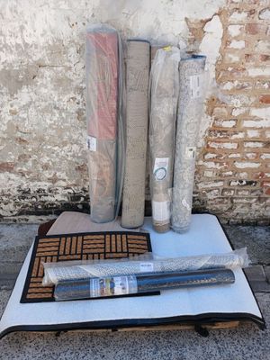 plusieurs rouleaux de tissu, un rouleau de moquette et un rouleau de toile posés par terre