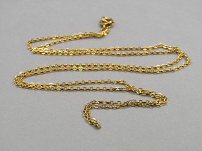 un collier en or avec une chaîne posée sur une surface grise