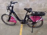 un vélo garé sur un parking, avec un sac rose à l'arrière