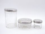 three glass jars with silver lids on a white surface