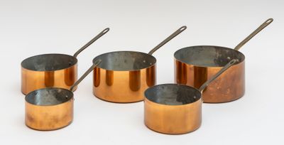 six casseroles et cuillères en cuivre sont alignées sur une surface blanche