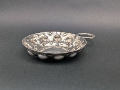an antique silver bowl with a handle on a black surface