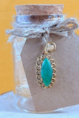 a small glass jar with a green stone pendant on it