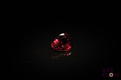 un gros plan d'un diamant rouge en forme de cœur sur une surface noire