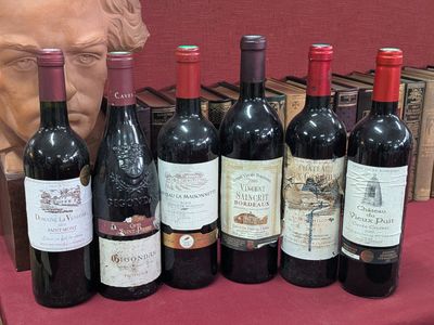 plusieurs bouteilles de vin posées sur une table à côté du buste d’un homme