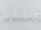 four clear wine glasses are lined up on a white surface