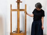 a woman standing next to a wooden easel in a room