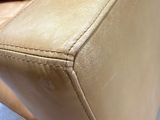 the back of a tan leather couch with a brown pillow