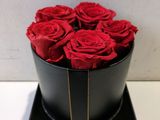 des roses rouges dans une boîte noire posée sur une table blanche