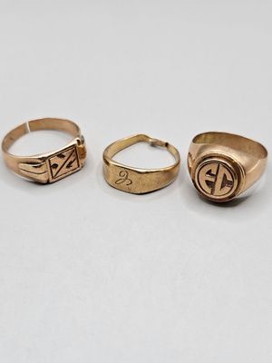three gold rings with initials on them sitting on a white surface