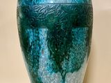 un vase bleu et vert posé sur une surface blanche