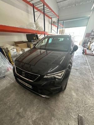 Une voiture noire est garée dans un garage, avec d'autres véhicules en arrière-plan.