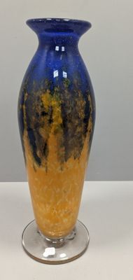 un vase bleu et jaune posé sur un socle en verre