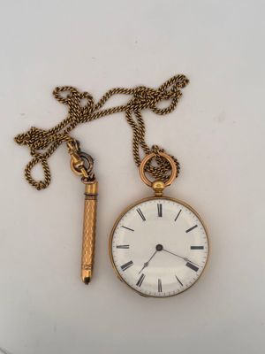 a gold pocket watch and a gold chain on a white surface