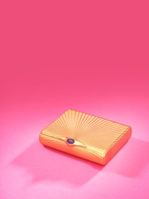 a gold clutch bag with a blue eye on a pink background