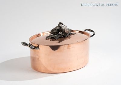 une grande casserole en cuivre avec un couvercle, posée sur un plan de travail blanc
