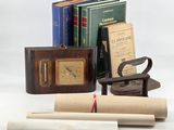 several books, a clock, a book case, and a pair of scissors sit on a white surface