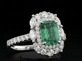un gros plan d'une bague sertie d'une émeraude verte et de diamants, posée sur une surface noire
