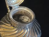 une théière en argent avec son couvercle, posée sur une table noire
