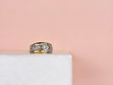 un gros plan d'une bague en or et diamants posée sur un bloc de marbre blanc