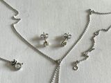 Ensemble collier et boucles d'oreilles en argent posé sur un fond blanc