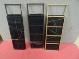 three black and gold bookshelves on a pink surface