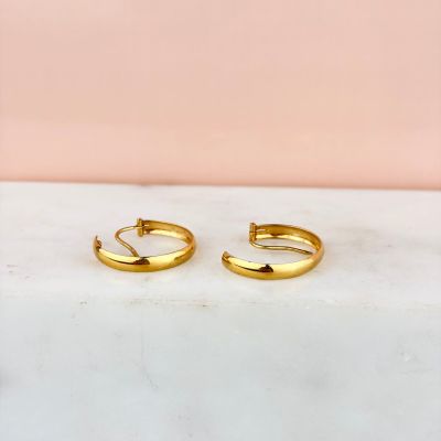 une paire de boucles d'oreilles créoles en or posée sur un comptoir en marbre