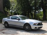 a silver mustang parked in a parking lot next to some trees