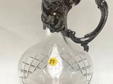 un vase en verre muni d'une poignée en argent, posé sur une table