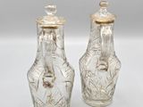 pair of clear glass vases with gold lids on a white surface