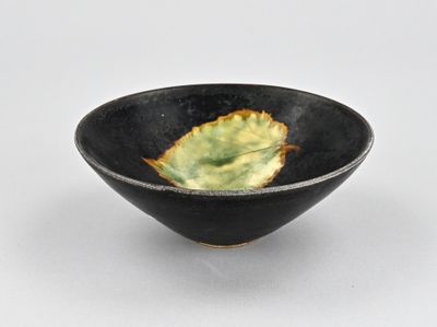 un petit bol noir contenant une feuille verte