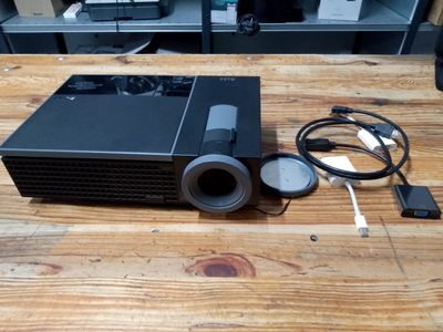 a small projector sitting on a wooden table next to a charger