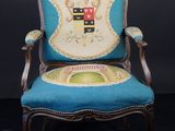 une vieille chaise dont l'assise est recouverte d'un tissu bleu et sur laquelle figure un blason