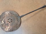 a metal strainer with a handle on the floor