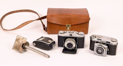 several old cameras and a leather case on a white surface
