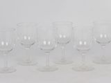 six empty wine glasses lined up in a row on a white surface