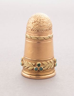 an image of a gold thimble with a green bead on it