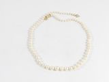 un collier de perles blanches avec un fermoir en or sur fond blanc