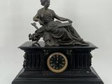 statue d'une femme assise sur une table, avec une horloge devant elle