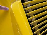 someone pointing to the front of a yellow car that is parked in a garage