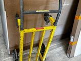 a yellow hand truck with a black handle next to a cardboard box